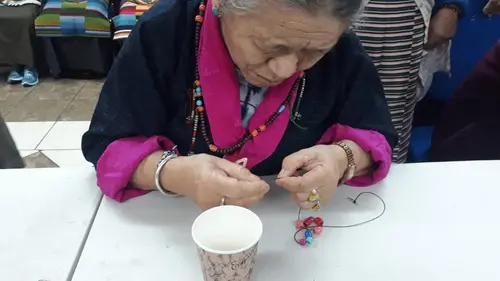 Elder woman crafting bead jewelry during an activity session