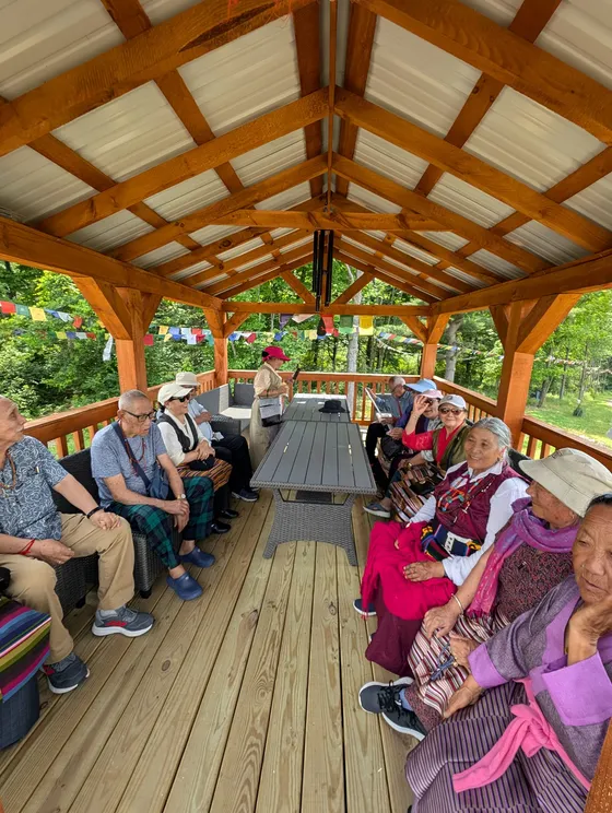 Elders gathering under prayer flags at a pavilion