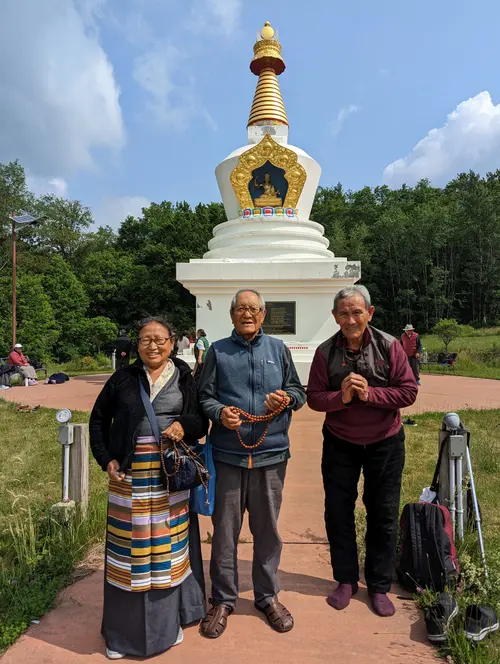 Three elders posing in front of a white stupa with prayer beads